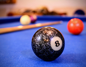 Bola de billar negra con el número 8, sobre una mesa de billar azul, con otras bolas visibles al fondo.