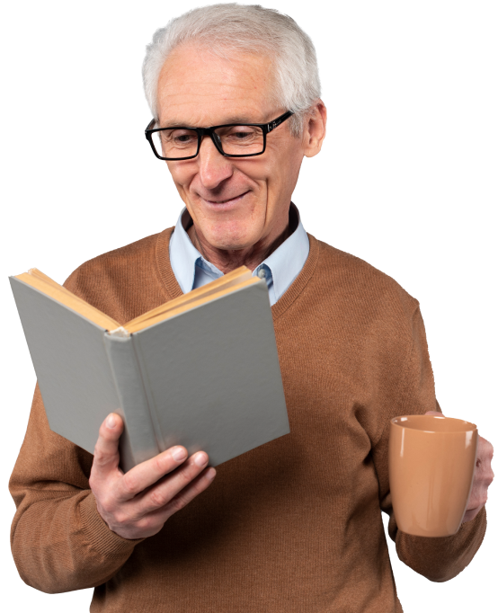 Hombre mayor con gafas, sosteniendo un libro gris en una mano y una taza en la otra, vestido con un suéter marrón, sonríe mientras lee. Fondo neutro.